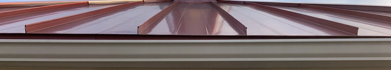 Burgundy standing-seam metal panels at an eave above a gutter