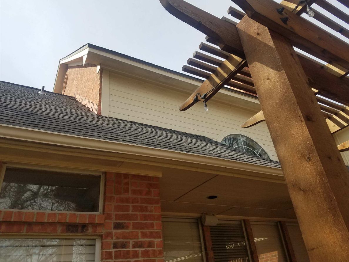 Finished asphalt shingle roof, gutter and eaves beside a wood pergola