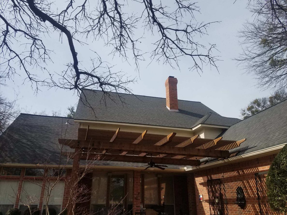 Completed shingle roof on a brick home with chimney and backyard pergola